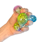 A hand squeezing a NeeDoh Press-Doh. The colorful doh is visible through the white and black designs of the exterior.